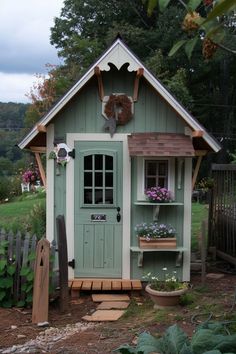 a small green shed with flowers in the window