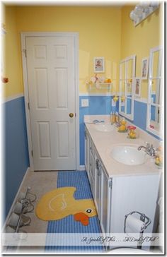 a bathroom with yellow rubber ducky rug on the floor and blue walls, along with two sinks