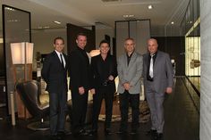 four men in suits are posing for a photo inside an office building, one man is wearing a suit and the other has his hands on his hips