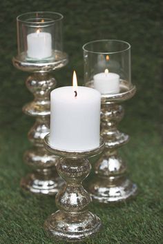 three clear glass candlesticks sitting on top of green grass