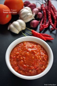 a white bowl filled with sauce next to garlic and red peppers