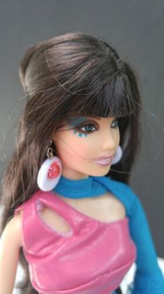 a close up of a doll wearing a pink dress and blue shirt with large earrings