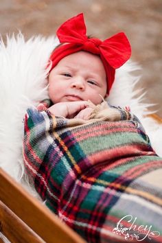 a baby wearing a red bow laying on top of a wooden bench in a blanket