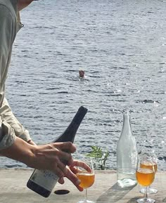 two glasses of wine are being poured in front of a man on the water's edge