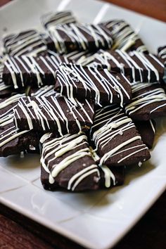 chocolate brownies with white drizzles on them are arranged on a plate