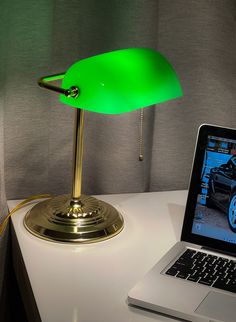 a laptop computer sitting on top of a white desk next to a green table lamp