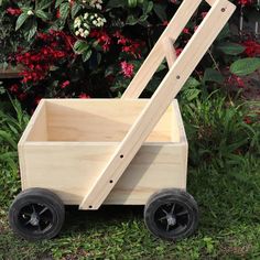 a wooden wagon sitting in the grass with wheels on each side and flowers behind it