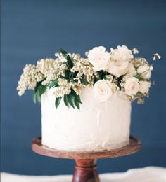 a white cake topped with flowers on top of a wooden stand