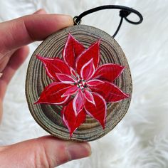 a hand holding a wooden ornament with a red flower on it