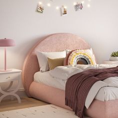 a bed with pink headboard and pillows in a white room next to a table