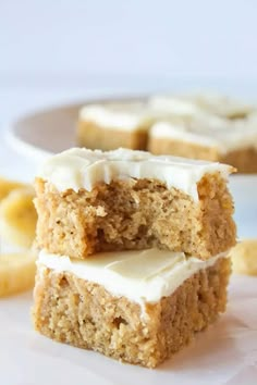 banana blondies with cream cheese frosting are stacked on top of each other in front of bananas