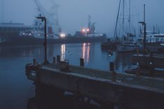 boats are docked in the harbor on a foggy day with lights reflecting off them