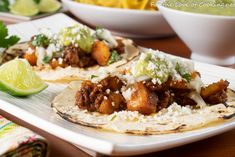 two tacos on a plate with lime wedges