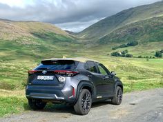 the rear end of a gray toyota c - hr driving down a country road with mountains in the background