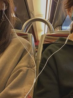 two people sitting on a bus with ear buds in their ears and one person wearing headphones