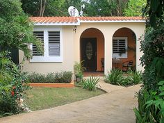 a small house with an orange roof and white shutters on the front door is surrounded by greenery