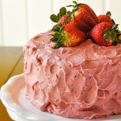 a cake with pink frosting and strawberries on top is sitting on a plate