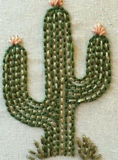 an embroidered cactus is shown on a piece of fabric with two small pink flowers in the center