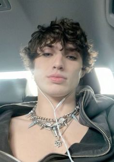 a woman with short hair wearing a black jacket and silver necklace on her neck in the back seat of a car