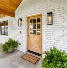 a white brick house with two planters and a door mat on the front porch