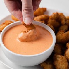 a person dipping something into a bowl of dip with tater tots on the side