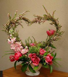 a heart shaped arrangement with pink flowers and greenery