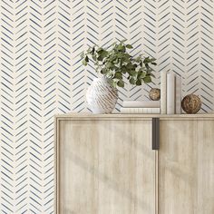 a white vase sitting on top of a wooden cabinet next to a wall with geometric designs