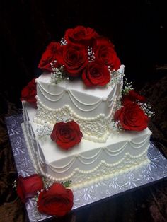 a three tiered wedding cake with red roses on top and pearls around the edges