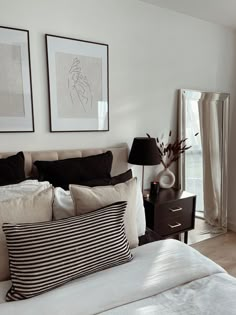 a bed with black and white pillows in a bedroom next to two pictures on the wall