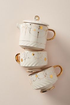 three white cups with gold rims are stacked on top of each other in the shape of mugs