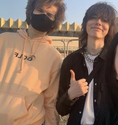 two young men wearing face masks standing next to each other with one giving the thumbs up