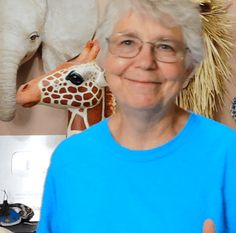 an older woman wearing glasses and a blue shirt standing in front of a wall with pictures of animals on it