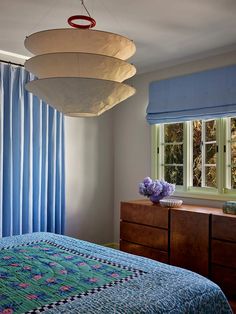 a bed room with a neatly made bed next to a window and a lamp hanging from the ceiling