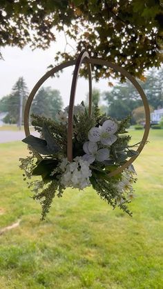 a flower arrangement hanging from a tree in the grass with a house in the background