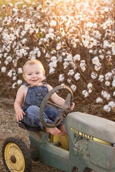 a little boy sitting on top of a tractor in front of some cotton plants and smiling