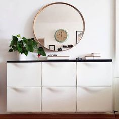 a white dresser with a round mirror above it and a potted plant on top