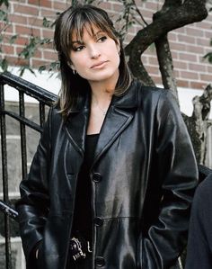 a woman wearing a black leather jacket standing in front of a tree