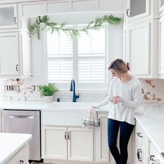 a woman standing at the sink in a kitchen with white cabinets and counter top space