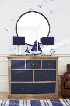 a living room with a brown chair and a blue dresser in front of a round mirror