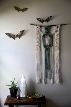 two butterflies are hanging on the wall next to a table with a plant and vase