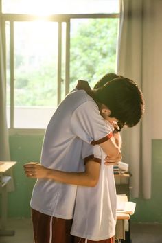 a man and woman hug each other in front of a window with sunlight streaming through the windows