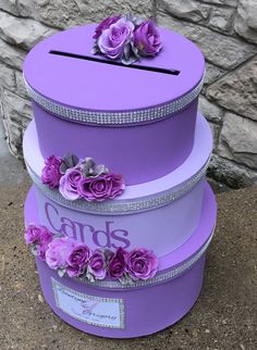 three purple boxes with flowers on them are stacked next to a brick wall and stone wall