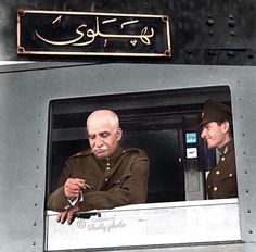 two men in uniform look out the window of a train car as another man looks on