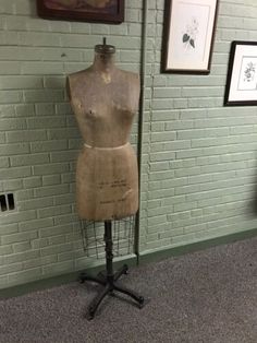 an old mannequin sitting on top of a stand in front of a brick wall