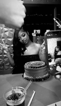 a woman sitting at a table with a cake in front of her and a cell phone