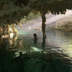 a person swimming in a pool with sunlight coming through the cave walls and water surrounding them