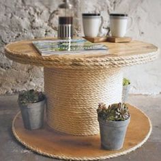 a rope covered table with two potted plants on it and coffee cups next to it