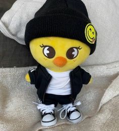 a yellow stuffed animal wearing a black hat and jacket with smiley face on it's head