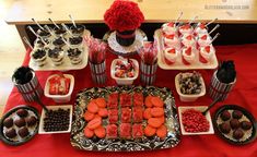 a table topped with lots of food and desserts on top of red cloth covered tables