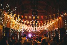 an indoor party with lights and bunting strung from the ceiling, people sitting at tables in front of them